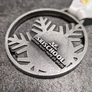 medaglia personalizzata skischool seiser alm alpe di siusi in metallo a rilievo 2D senza smalti finitura argento antico con nastro personalizzato in sublimazione vista laterale