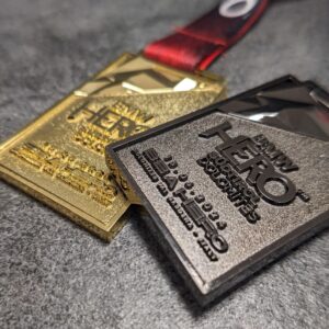 medaglia personalizzata hero in metallo a rilievo 3D senza smalti finitura oro e nichel nero con fondo satinato e rilievi lucidi con nastro personalizzato in sublimazione