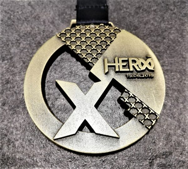 Hero X 2019 customised medal in embossed 2D perforated metal with antique bronze finish and personalised sublimation ribbon