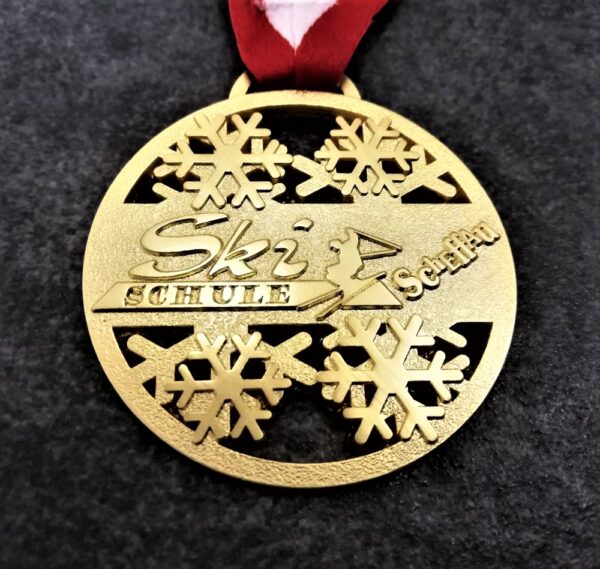 customised Ski Schule Scheffau medal in embossed 2D perforated metal with satin gold finish and red-white ribbon