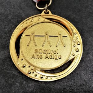 customised Sport Scholastic Sudtirol Alto Adige medal in embossed 2D perforated metal with polished and satin gold finish and red and white ribbon