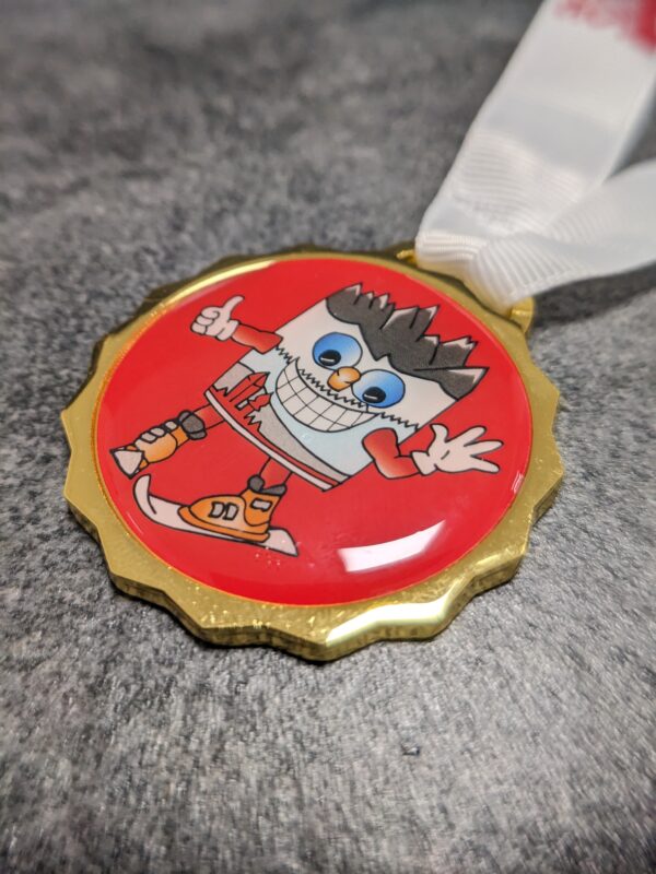 custom san candido ski school medal in gold finish silk screen printed metal with lens effect and personalized screen printed ribbon side view