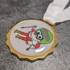 custom skischool san candido medal in gold finish silk screened metal with lens effect and personalized silkscreen ribbon side view