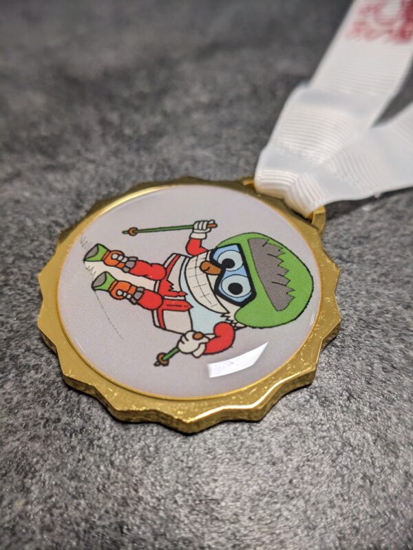 custom skischool san candido medal in gold finish silk screened metal with lens effect and personalized silkscreen ribbon side view