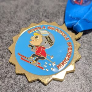 custom skischool speikboden medal in 2D gold finish enameled metal with lens effect and personalized sublimation ribbon side view