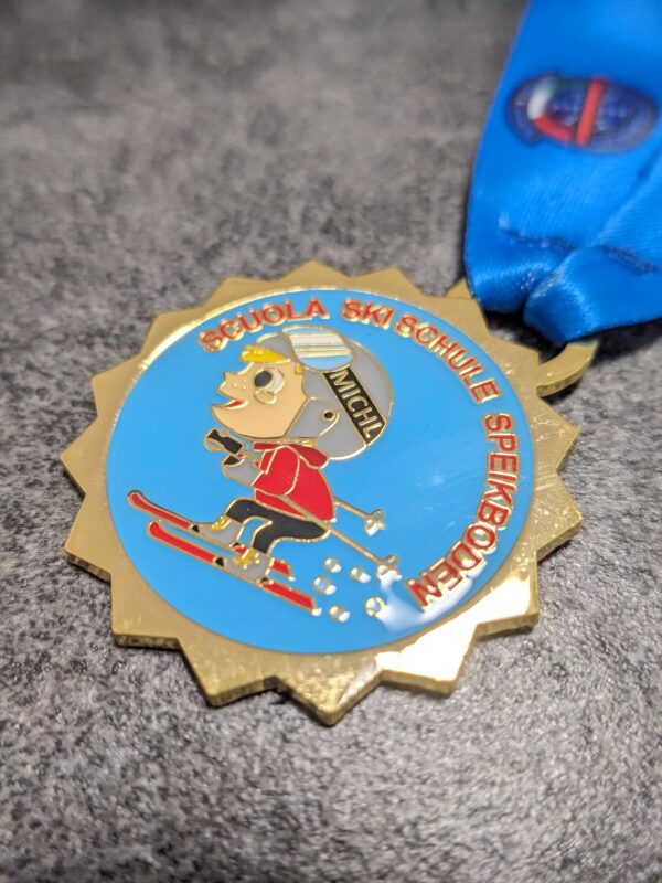 custom skischool speikboden medal in 2D gold finish enameled metal with lens effect and personalized sublimation ribbon side view